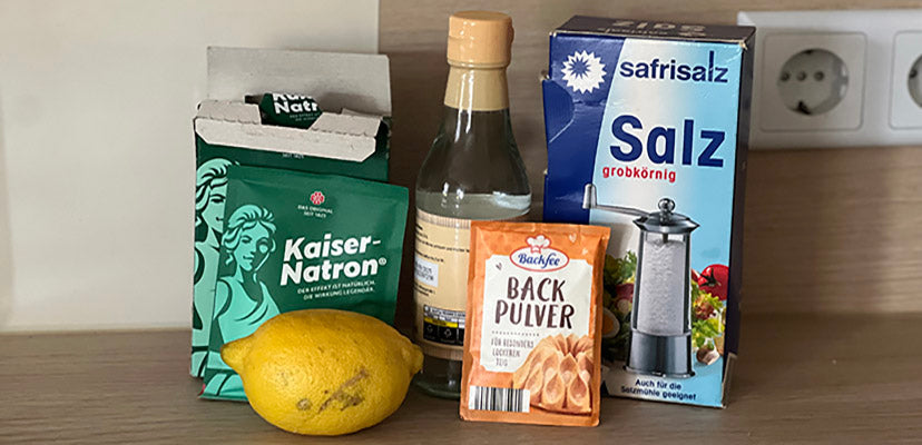 Verschiedene Hausmittel zur Zahnprothesenreinigung stehen versammelt da, wie Zitrone, Natron, Backpulver, Essig, grobkörniges Salz uvm.