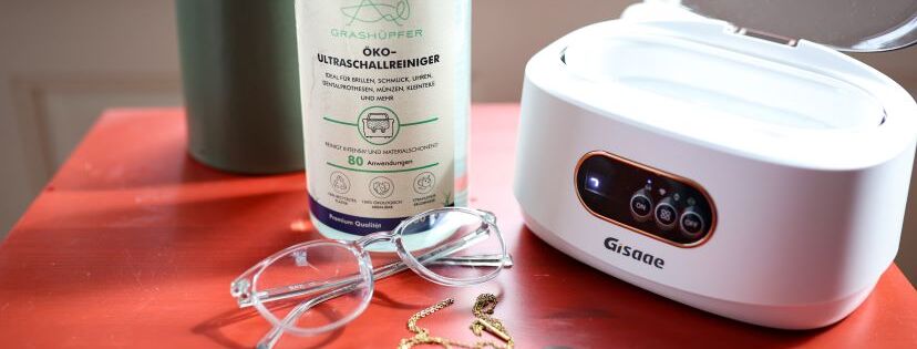 Ein Ultraschallreinigungsgerät steht neben einer Brille und dem Grashüpfer Öko-Ultraschallreiniger für Ultraschallgeräte im Zusammenhang mit dem Thema Ultraschallreiniger für Brillen.