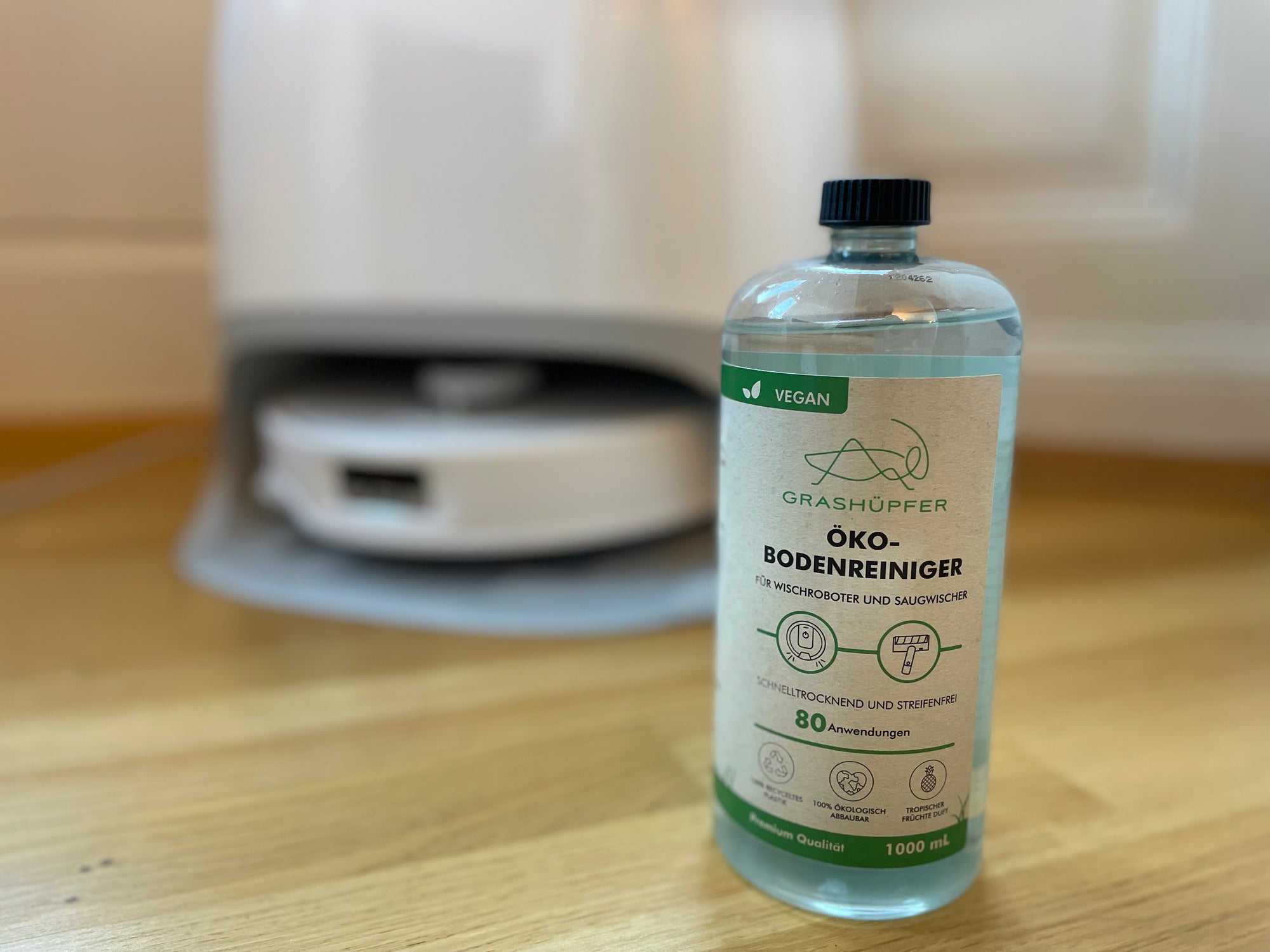 Der Öko-Bodenreiniger von Grashüpfer steht neben einem Wischroboter.