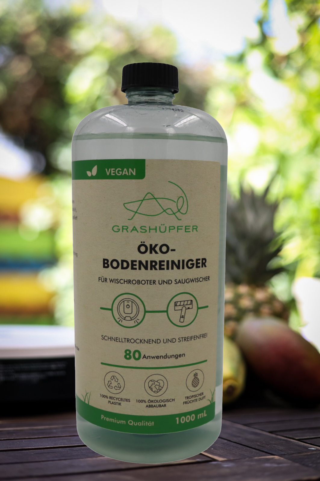 Der Öko-Bodenreiniger von Grashüpfer steht neben einem Wischroboter und dahinter liegen Früchte, was für einen frischen, angenehmen und fruchtigen Duft steht.