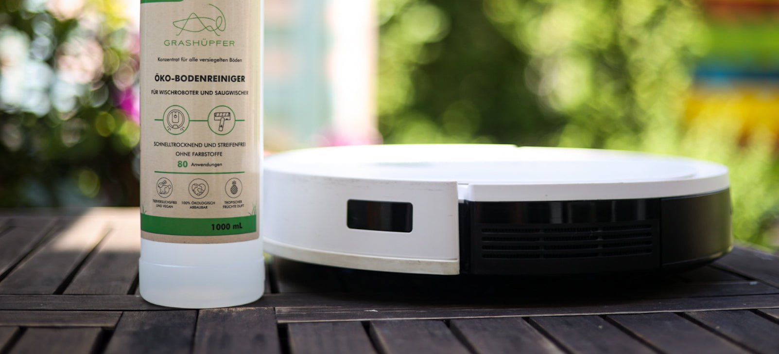 Der Grashüpfer Öko-Bodenreiniger für Wischroboter und Saugwischer steht neben einem Wischroboter.