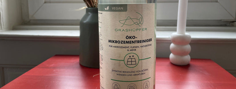 Der Grashüpfer Öko-Mikrozementreiniger für Mikrozement, Fliesen und Natursteine steht auf einem Tisch und dient zur richtigen Pflege von Mikrozement.