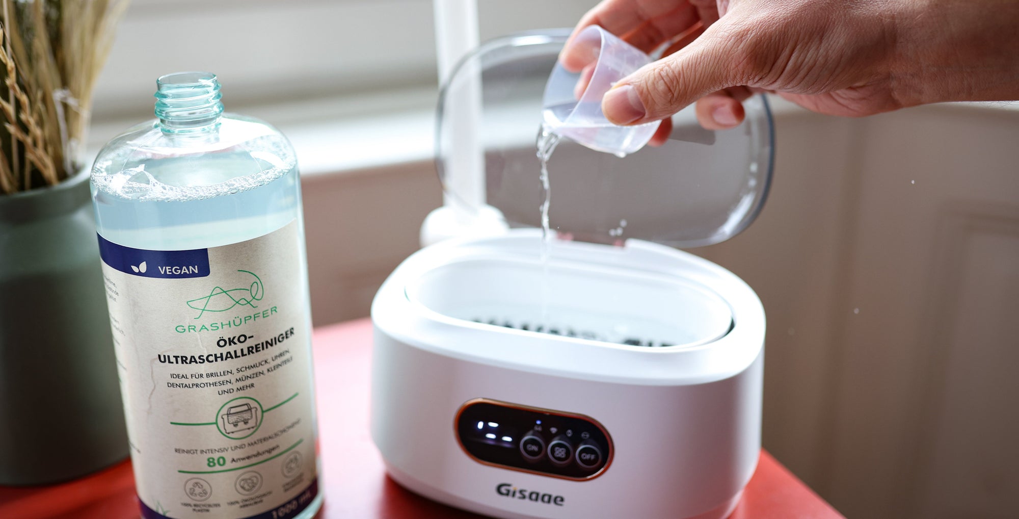 Die Ultraschallreinigungsflüssigkeit wird in ein Ultraschallreinigungsgerät geschüttet und daneben steht der GrashüpferÖko-Ultraschallreiniger für Ultraschallgeräte.