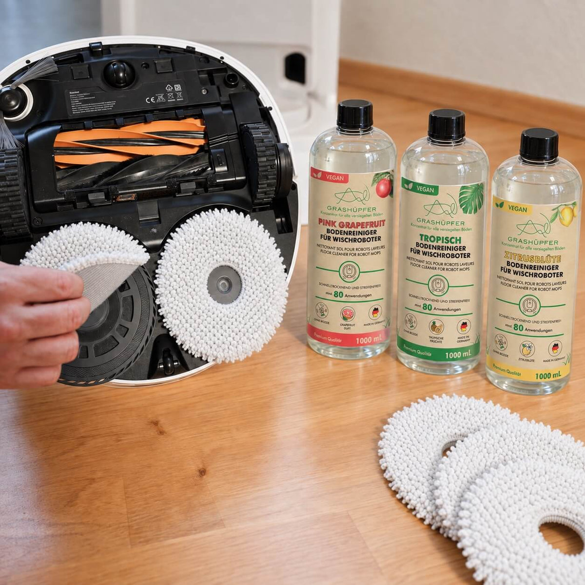 ECOVACS Wischroboter mit drei Grashüpfer Bodenreinigern für Wischroboter sowie austauschbaren Wischpads bei der Zubehöranwendung.