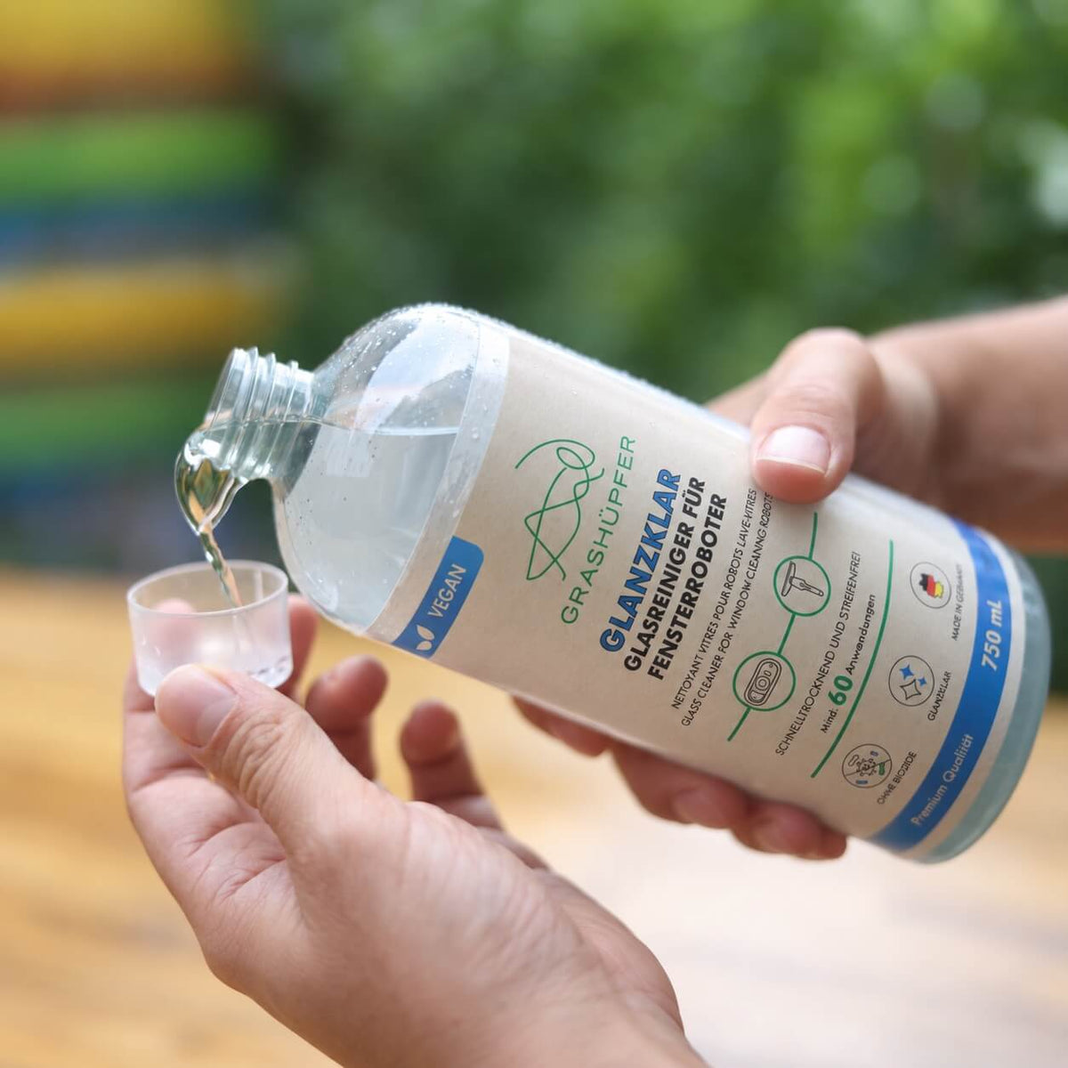 Glanzklar Glasreiniger für Fensterroboter von GRASHÜPFER wird aus der 750-ml-Flasche in einen Messbecher dosiert.
