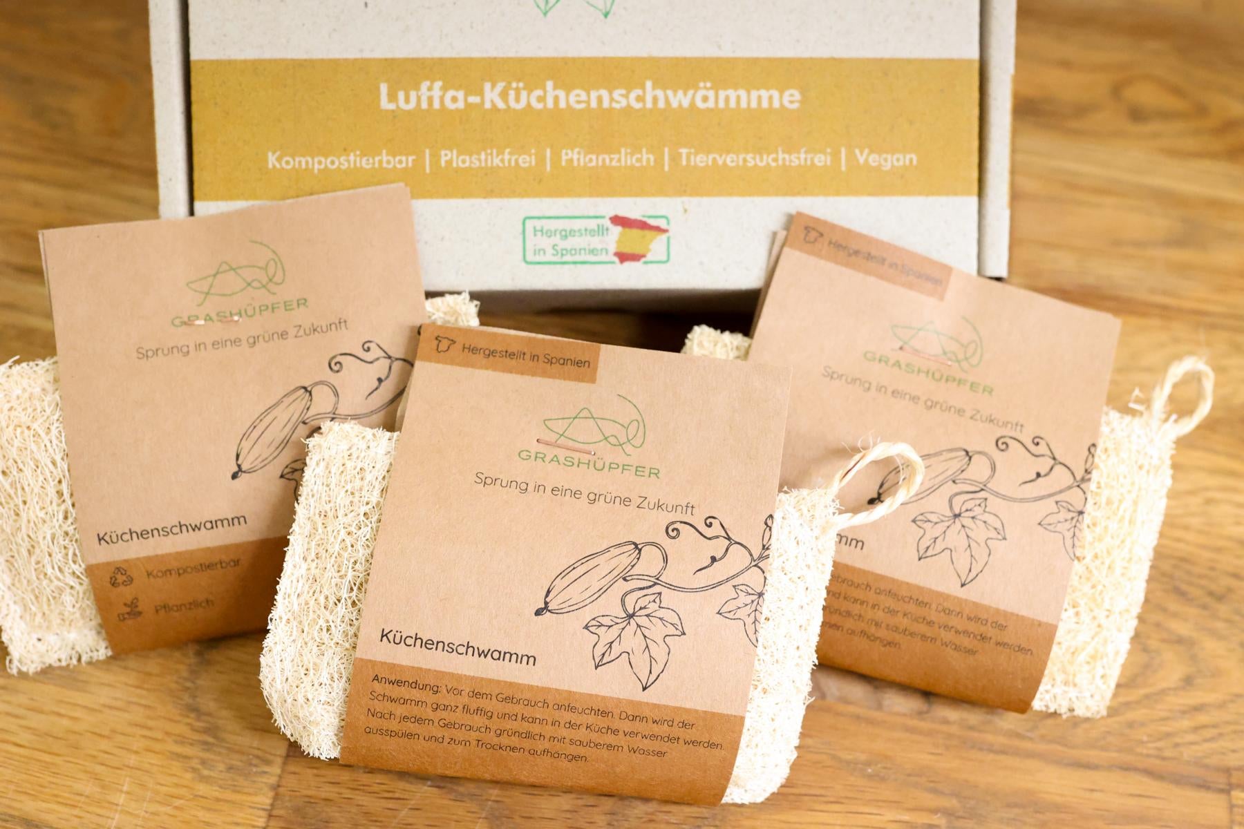 Das Grashüpfer 3er-Set Luffa-Schwämme liegt in der Nahaufnahme neben der nachhaltigen Verpackung.