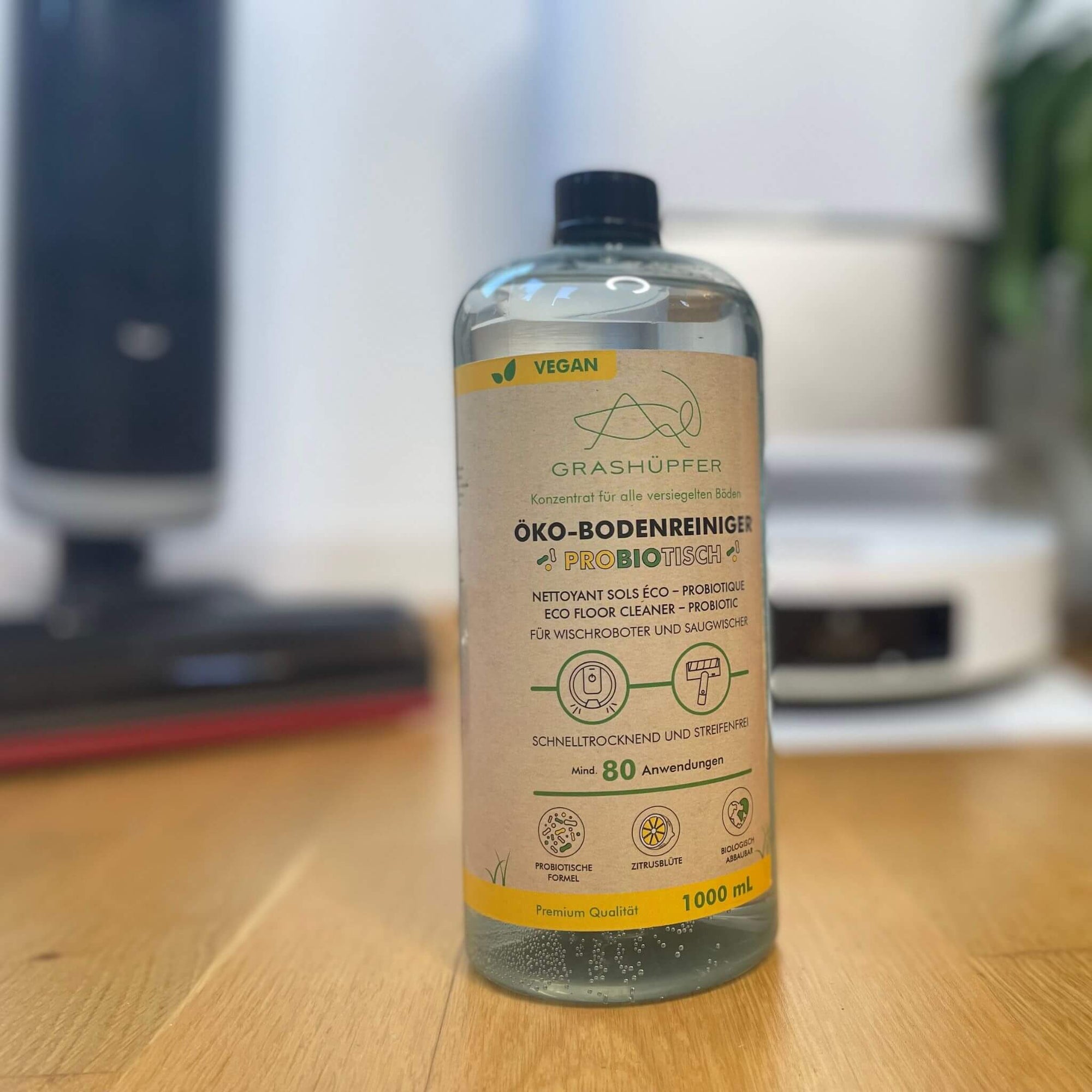 Moderne Wischroboter und Akkuwischsauger im Hintergrund, der probiotische Öko-Bodenreiniger auf einem Holzboden – perfekte Kompatibilität ohne Schaumbildung.