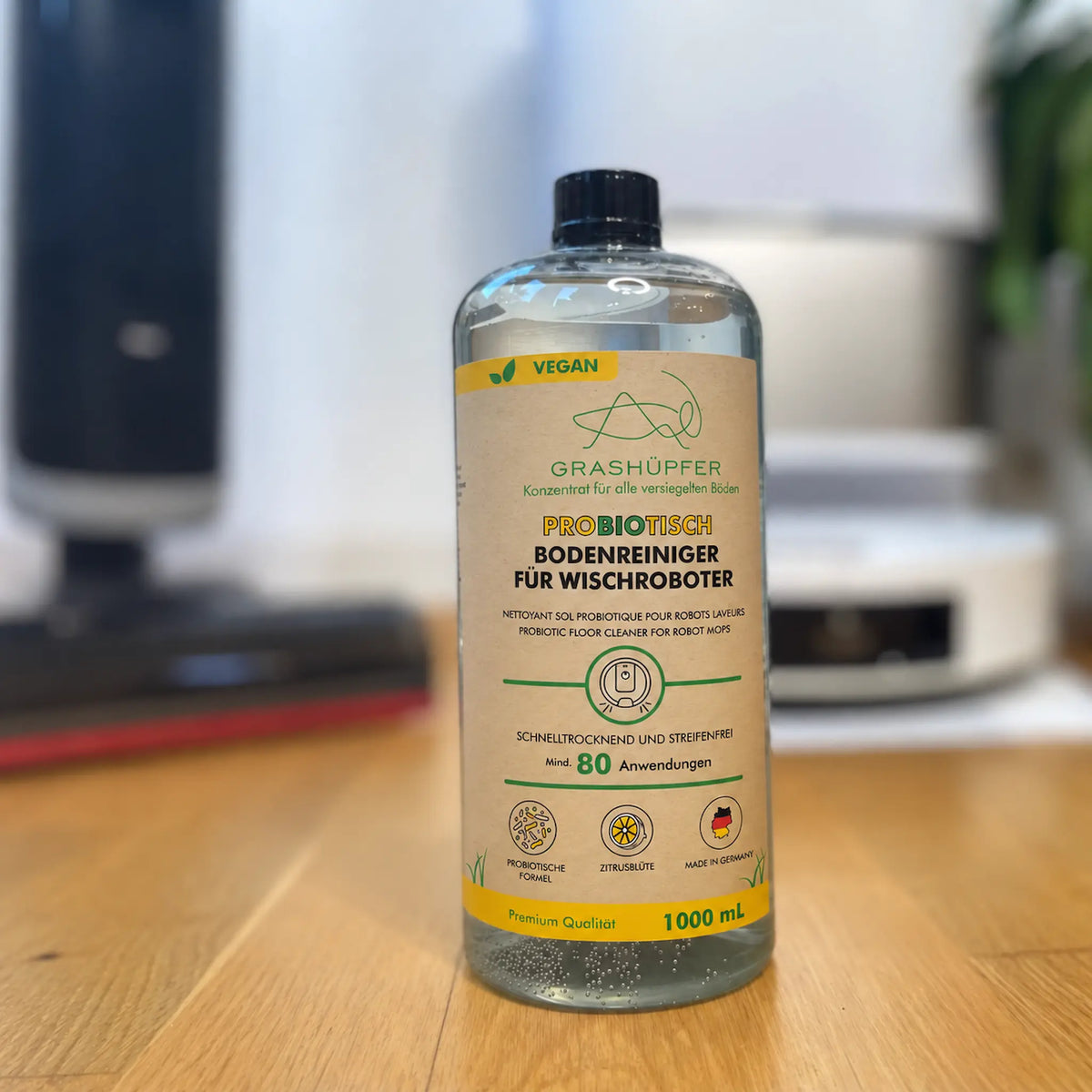 GRASHÜPFER probiotischer Bodenreiniger für Wischroboter Zitrusblüte auf Holztisch mit Saug-Wischrobotern im Hintergrund.