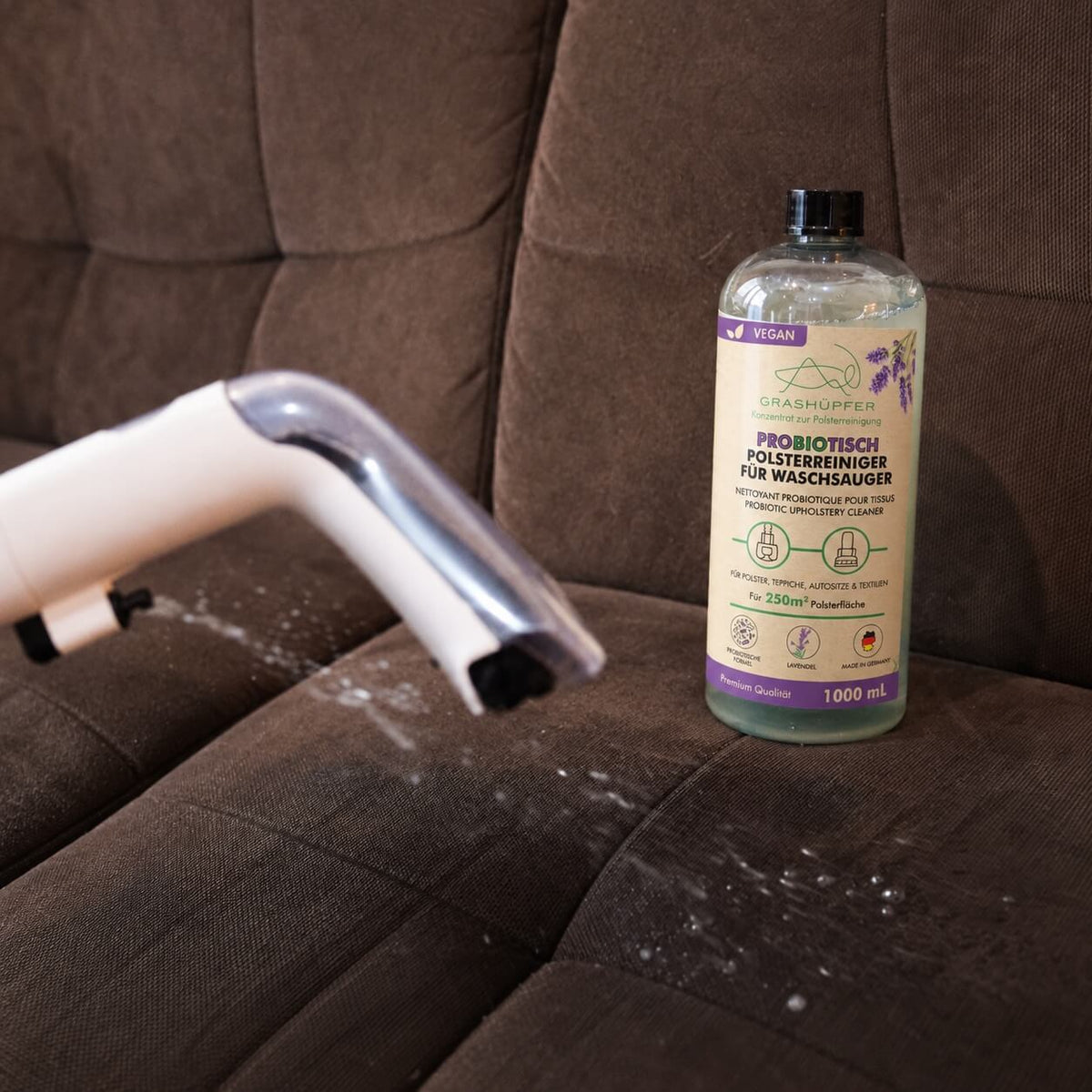 GRASHÜPFER probiotischer Polsterreiniger für Waschsauger neben einer Polsterdüse bei der Reinigung eines braunen Sofas.