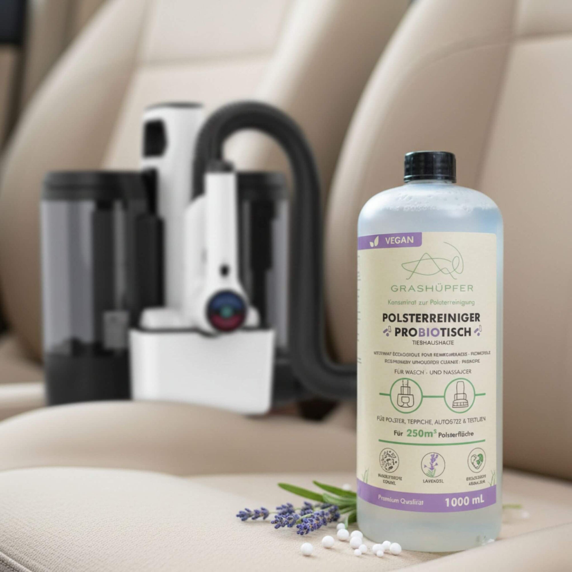 Der Probiotische Öko-Polsterreiniger & Geruchsentferner von Grashüpfer ist in der 1000ml Flasche zu sehen, daneben liegt Lavendel und ein Waschsauger für Polster ist im Hintergrund zu sehen.