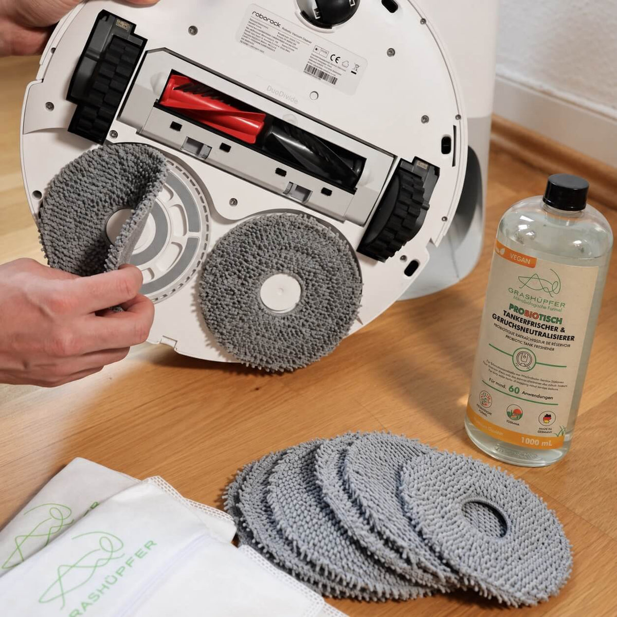 GRASHÜPFER probiotischer Tankerfrischer Toskana neben Roborock Saug-Wischroboter, grauen Wischpads und wiederverwendbaren Staubbeuteln.