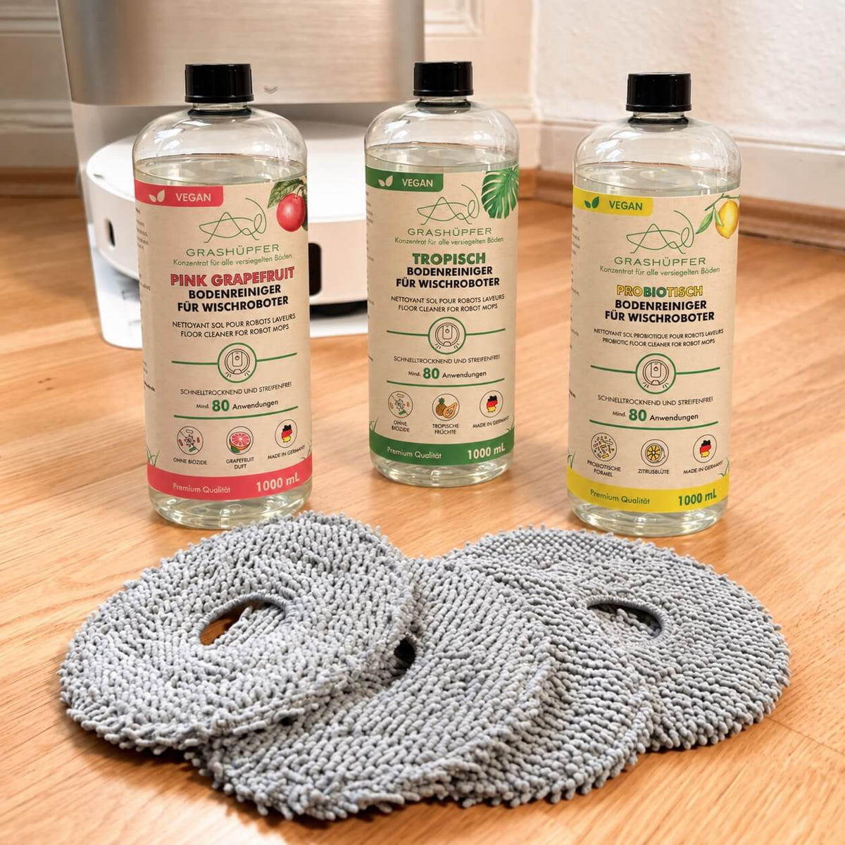 Grashüpfer Bodenreiniger und probiotischer Bodenreiniger mit mehreren Wischpads vor einer Dreame Reinigungsstation.
